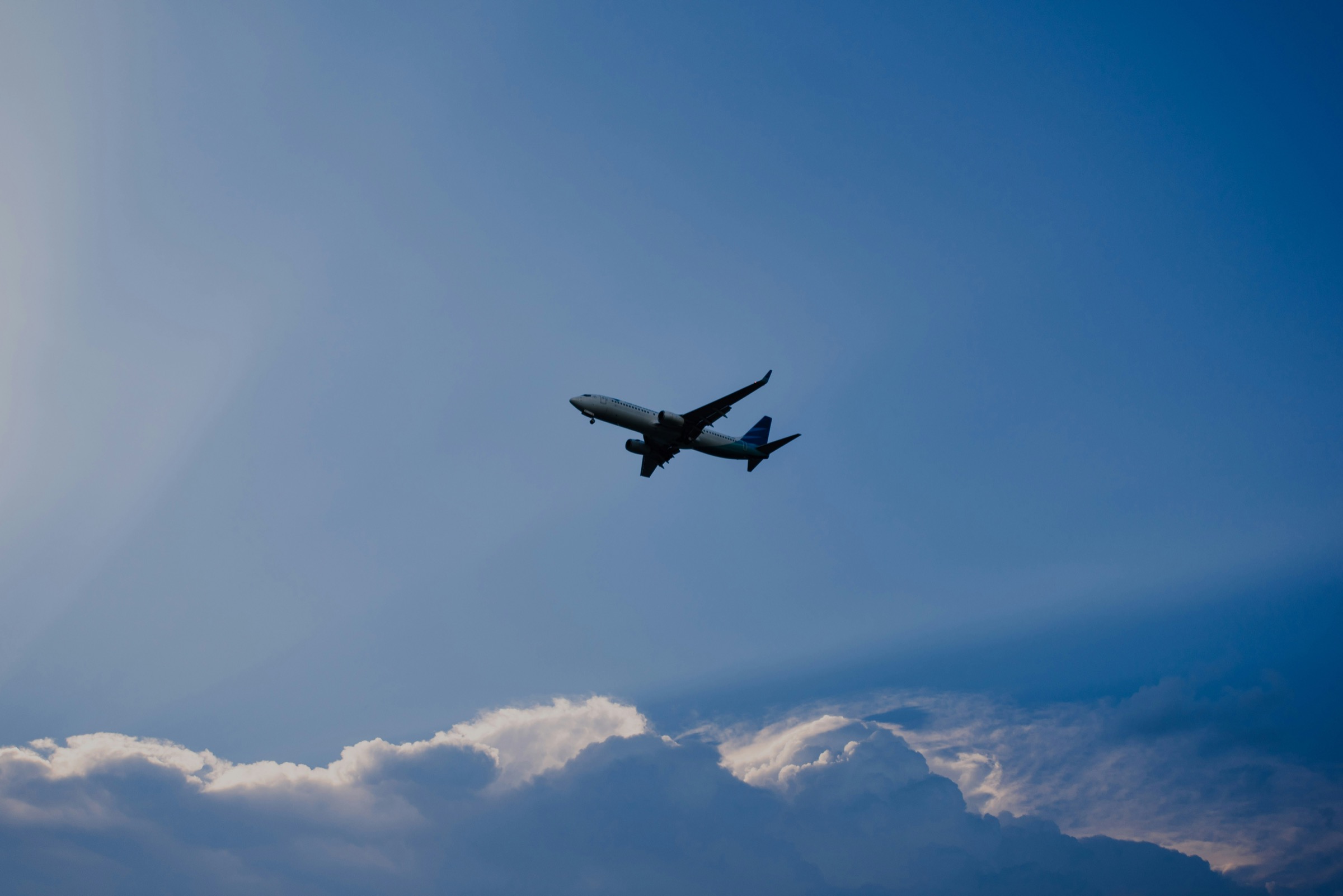 A jet climbing against a wide evening sky, seen from the ground looking straight up, clouds banked below it